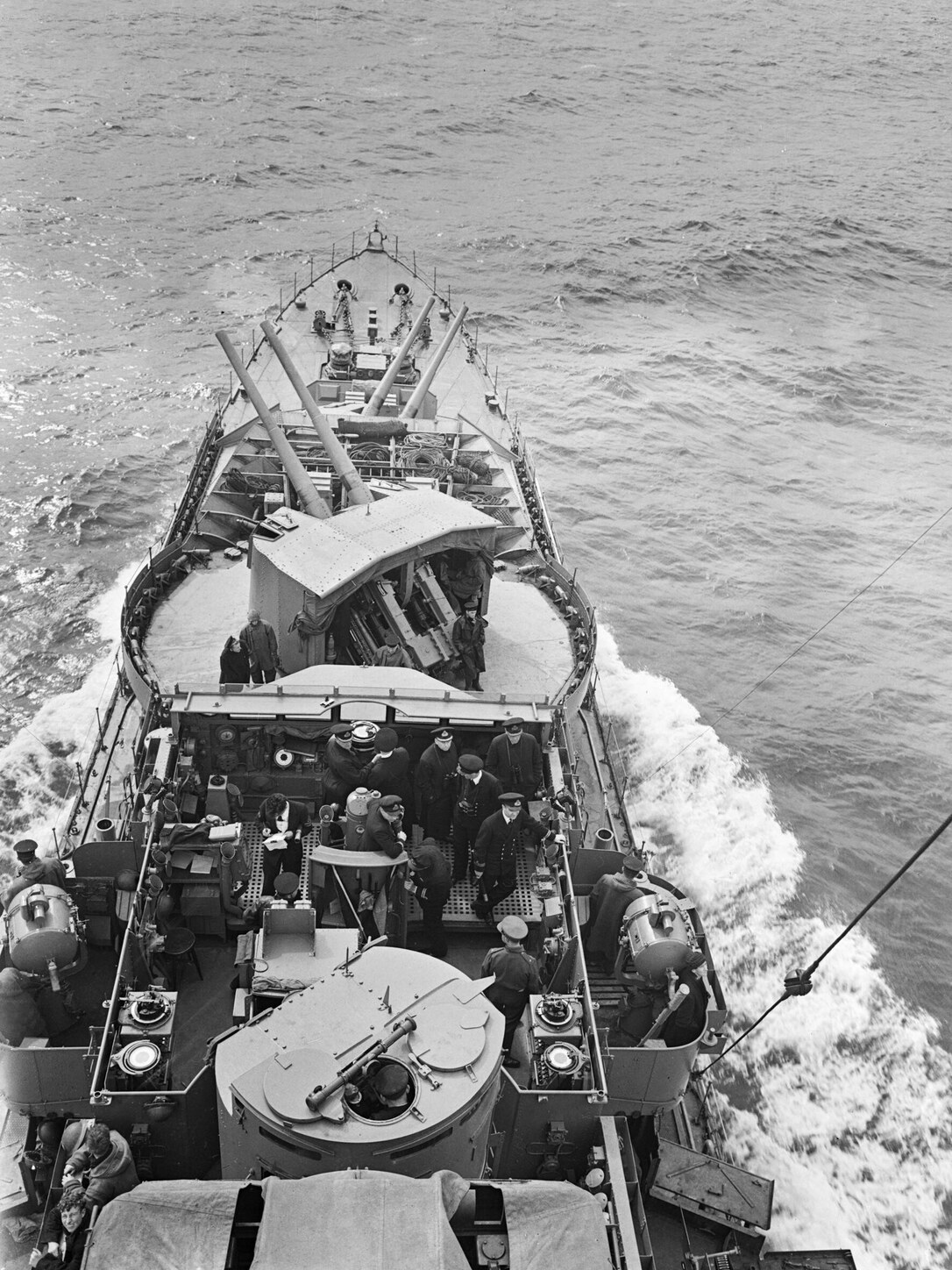 Looking down over HMS Kelvin's bridge and forecastle: officers and ratings at their stations, including a man writing at the bridge table
